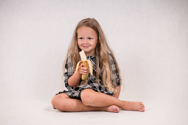 白い背景でおいしい健康的なバナナを食べて美しいかわいい女の子 - 写真・画像