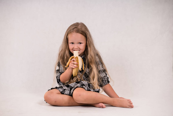 beautiful cute little girl eating delicious healthy banana on white background - Photo, Image