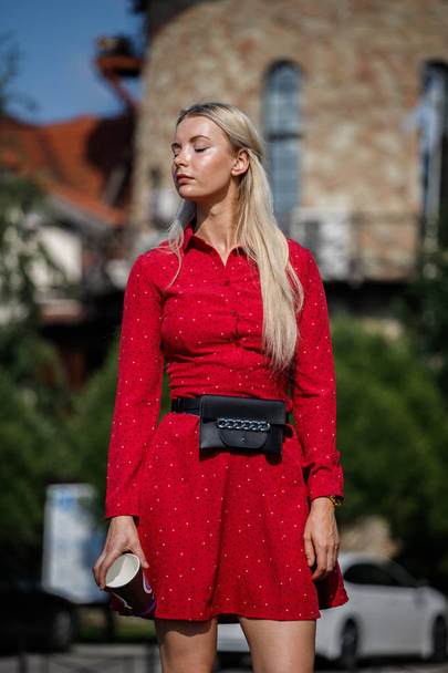 Outdoor fashion portrait of beautiful blond woman in red dress holding coffee cup, street background  - Φωτογραφία, εικόνα