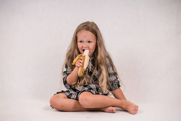 piękny Ładna dziewczynka jedzenie pyszne zdrowe banana na białym tle - Zdjęcie, obraz