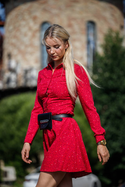Outdoor fashion portrait of beautiful blond woman in red dress standing on city street at daytime - Фото, изображение