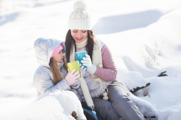 Mãe e sua filha se divertindo ao ar livre no inverno. Bonita família beber chá e cacau
 - Foto, Imagem