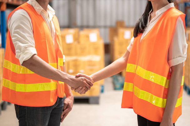 Warehouse operator teamwork. Male and female warehouse operators shaking hand. Warehouse in background. - Foto, imagen