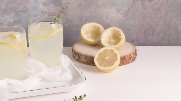 Cold lemonade or alcoholic cocktail with lemon, rosemary and ice in glass glasses on a light background. - Video