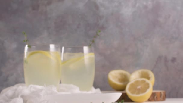 Cold lemonade or alcoholic cocktail with lemon, rosemary and ice in glass glasses on a light background. - Materiał filmowy, wideo