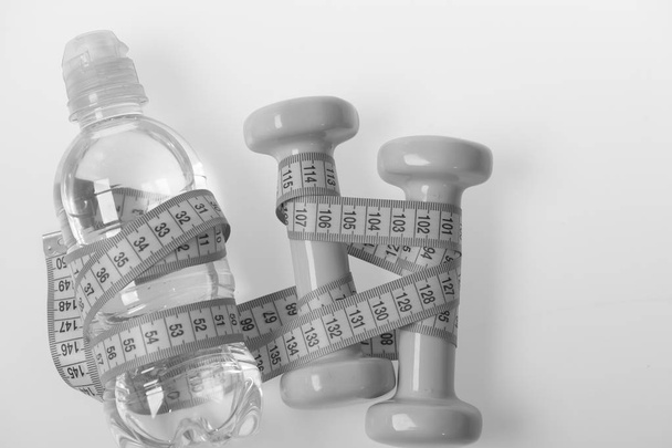 Dumbbells and water in cyan tape measure on white background, top view. Water bottle and barbells tied with blue measure tape - Fotó, kép