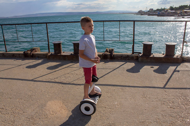 Child on hover board. Kids riding scooter in summer near the sea. Balance board for children. New modern technologies of eco transport. - Photo, Image
