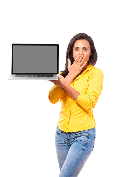 Mujer conmocionada sosteniendo un portátil en blanco en exhibición al espectador en su mano mientras se cubre la boca con su otra mano aislada en blanco
 - Foto, Imagen