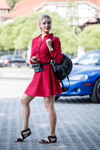 Outdoor fashion portrait of beautiful blond woman in red dress holding mobile phone, blurred street background  - Photo, Image