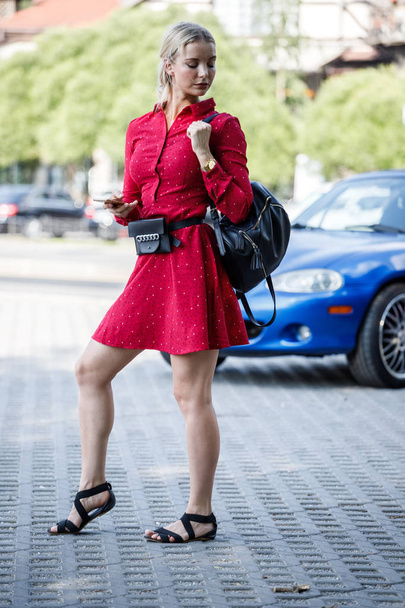 Outdoor fashion portrait of beautiful blond woman in red dress holding mobile phone, blurred street background  - Fotó, kép