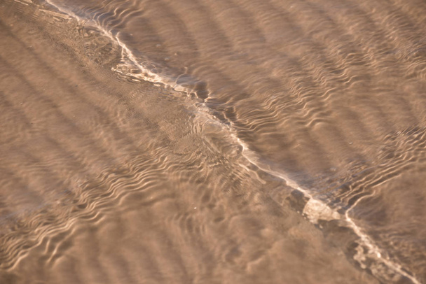 Homok háttér textúra a víz alatt. Átlátszó vízhullám, homokhullámok és napfény. Tengerfenék háttér - Fotó, kép