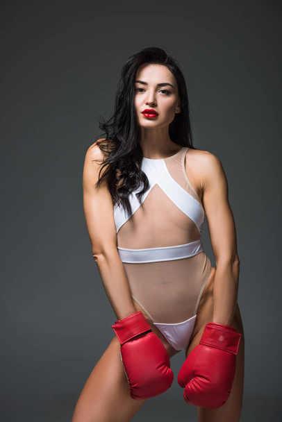 sexy beautiful sportive woman in white sportswear and boxing gloves looking at camera isolated on grey - Foto, afbeelding