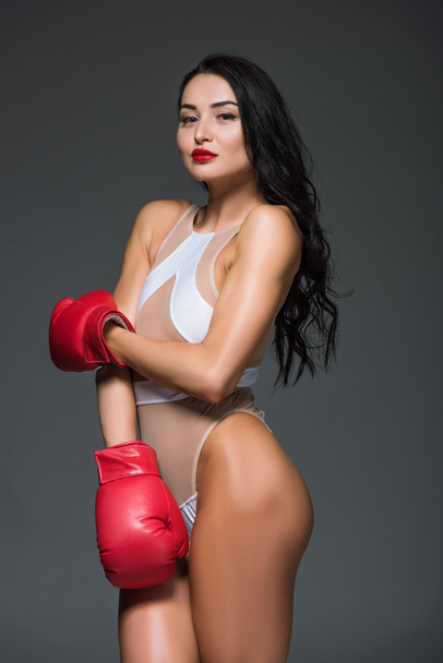portrait of sexy sportive woman in white leotard and boxing gloves isolated on grey - Photo, image