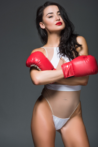atractiva mujer deportiva en maillot blanco y guantes de boxeo de pie con brazos cruzados aislados en gris
  - Foto, Imagen