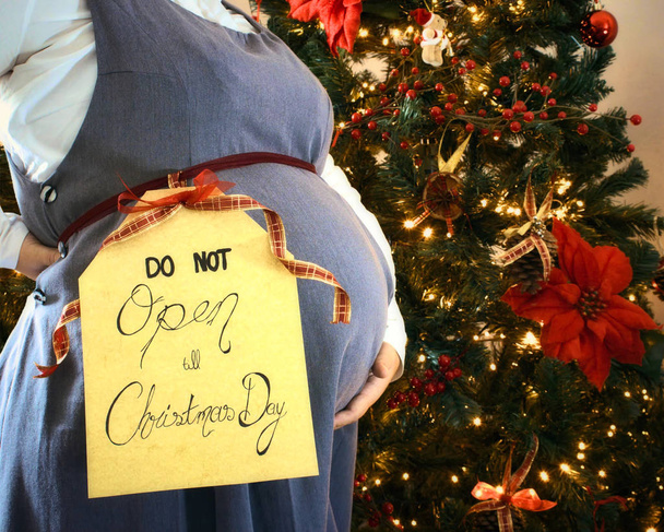 Raskaana oleva nainen osoittaa vatsa joulukuusi ja "Älä avaa vasta joulupäivänä" merkki
 - Valokuva, kuva