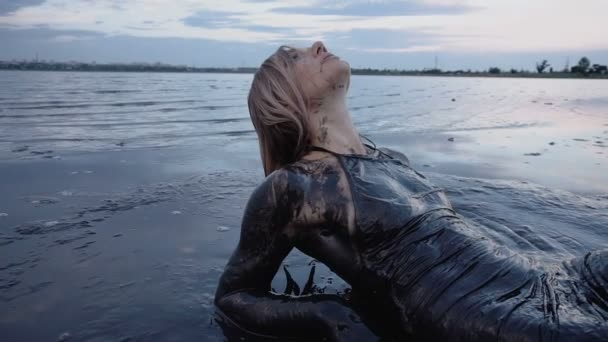 Αξιολάτρευτο λεπτή ξανθιά βάζει πασαλειμμένος σε μια μαύρη λάσπη μοιάζει με πετρέλαιο - Πλάνα, βίντεο