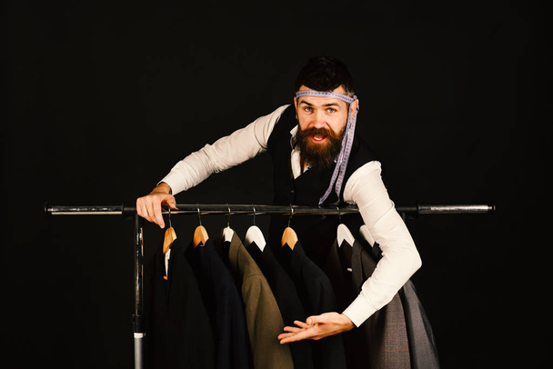 Fashion choice concept. Designer leans on clothes hangers. Man with beard in vest - Φωτογραφία, εικόνα