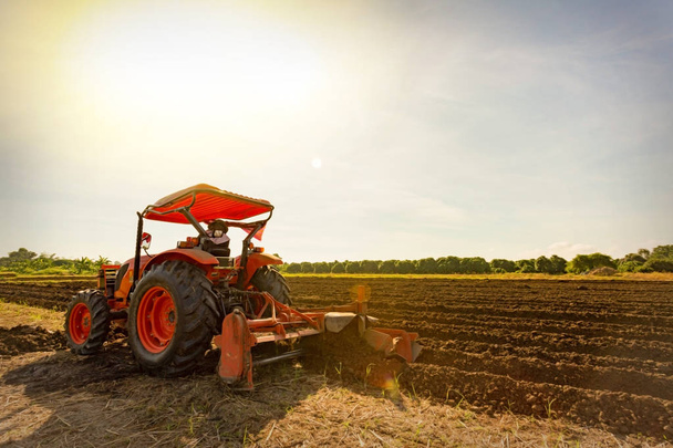 Close-up of agriculture red tractor cultivating field over blue sky - Photo, Image