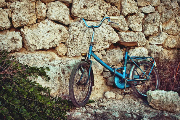 Velha bicicleta vintage azul encostada a uma parede de pedra ao sol no Mediterrâneo
 - Foto, Imagem