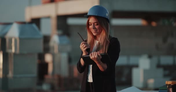 Young pretty female on construction site speaking using a radio and analyzing the plan of construction , at the end happy jumping. - Video, Çekim