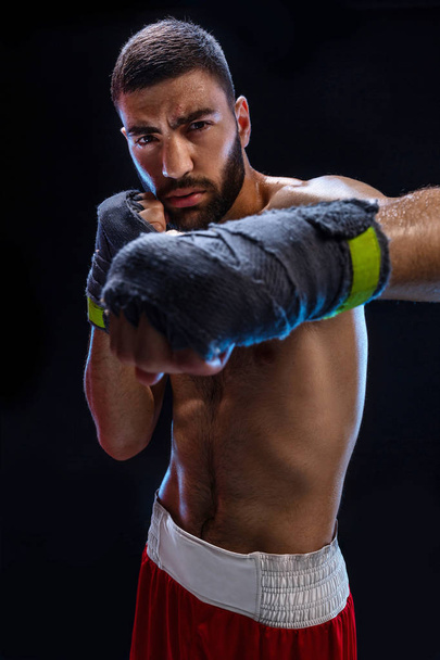 Боксер готов нанести мощный удар. Фото мускулистого человека с сильными руками и сжатыми кулаками в синих полосах на черном фоне
. - Фото, изображение