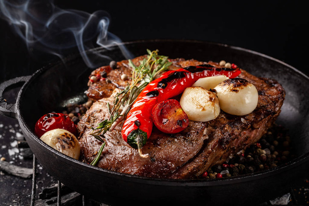concept of the process of cooking meat. The steak is roasted on charcoal in a cast-iron frying pan, with spices, garlic, hot red pepper, squarish, thyme. image background. Copy space, selective focus - Photo, Image