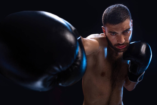 El hombre está golpeando a un oponente. Luchador enfocado con torso desnudo y guantes de boxeo mirando a la cámara. Ganar
. - Foto, Imagen