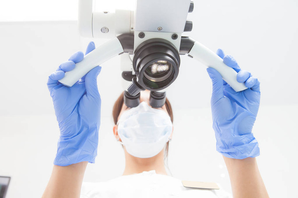 A female dentist is looking into a dental microscope. Bottom view. Focus on the microscope - Foto, afbeelding
