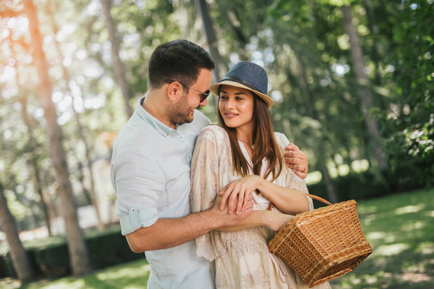 Cheerful young couple having fun and laughing together walking with basket in park - 写真・画像