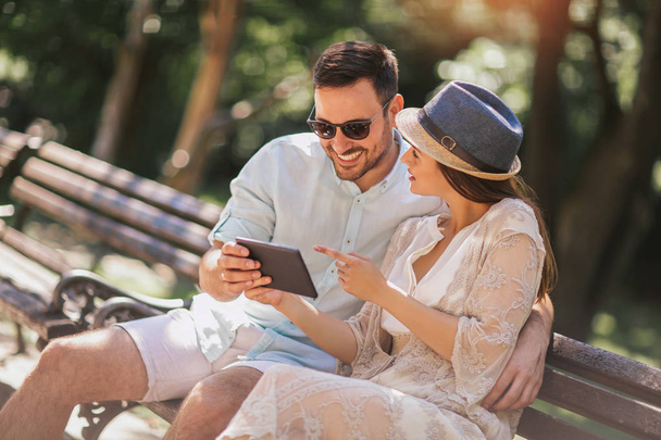Happy couple watching media using digital table sitting in park - Фото, зображення