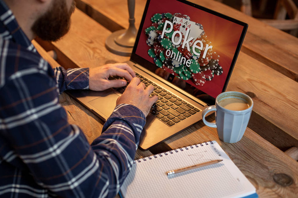 Молодой человек играет в покер через нетбук во время перерыва в кафе, мужчина сидит перед открытым компьютером ноутбука
. - Фото, изображение