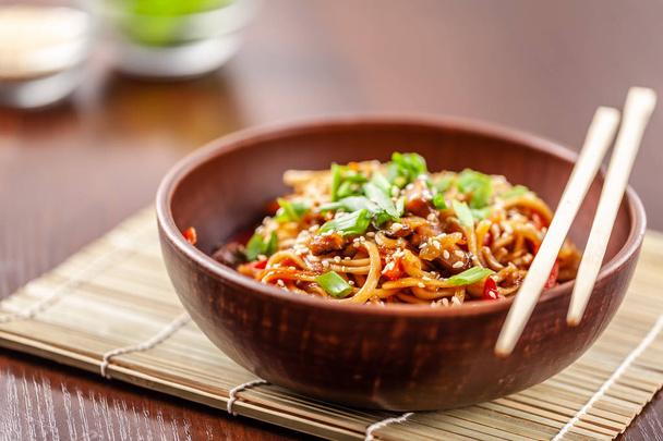 Asian Oriental Cuisine. Japanese noodles with chicken and vegetables, sesame and parsley, in a plate of red clay, stands on a table in a restaurant. Copy space, selective focus - Foto, imagen