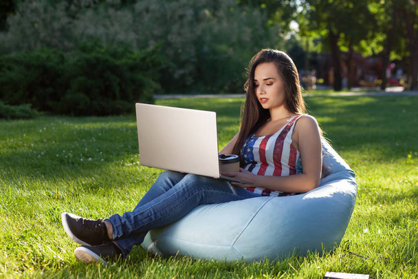 Fiatal, csinos lány laptop, Babzsák, kert és park, a zöld fű ülni. Online vásárlás koncepció - Fotó, kép