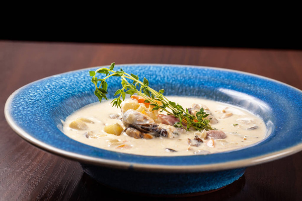 The concept of Italian cuisine. Creamy soup with seafood, mussels, potatoes, carrots, thyme. serve in a blue plate. - Photo, Image