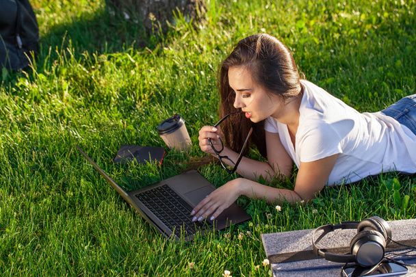 Giovane donna che utilizza il computer portatile nel parco sdraiato sull'erba verde. Tempo libero concetto di attività. - Foto, immagini