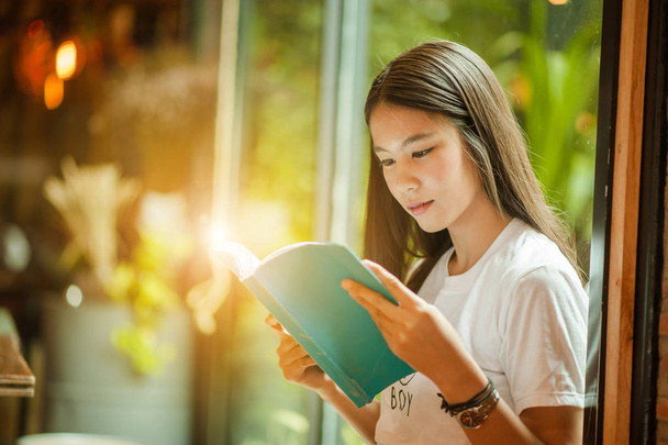 Молодая женщина в ресторане читает книгу. молодая женщина сидит дома, сидя у окна, расслабляясь в своей гостиной читая книгу
 . - Фото, изображение