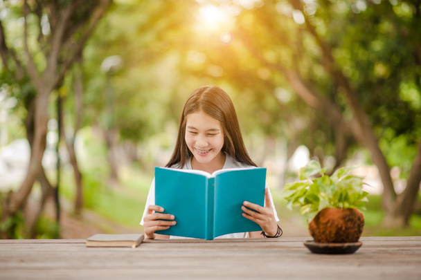 Libro de lectura de chicas asiáticas en el parque en verano de luz del sol. Libro de lectura de mujeres asiáticas en Tailandia. Una mujer hermosa asiática leyendo un libro a la mesa. - Foto, Imagen