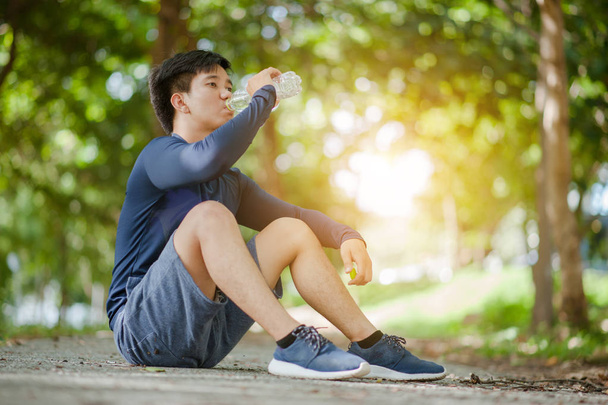 Asians man drinks water from a bottle after running in the park. - Photo, Image