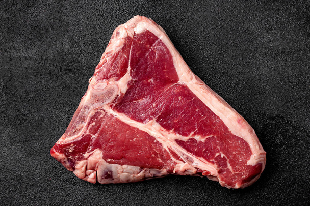 Vlees rauwe biefstuk ligt op een zwarte achtergrond. zijaanzicht, kopie ruimte, bovenaanzicht - Foto, afbeelding