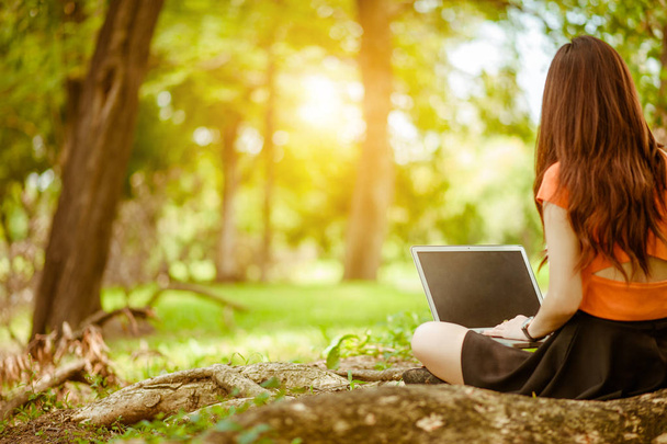  mujer sentada en el parque en la hierba verde con el ordenador portátil, portátil, manos en el teclado. Una maqueta de la pantalla del ordenador. Estudiante estudiando al aire libre. Copiar espacio para texto
 - Foto, imagen