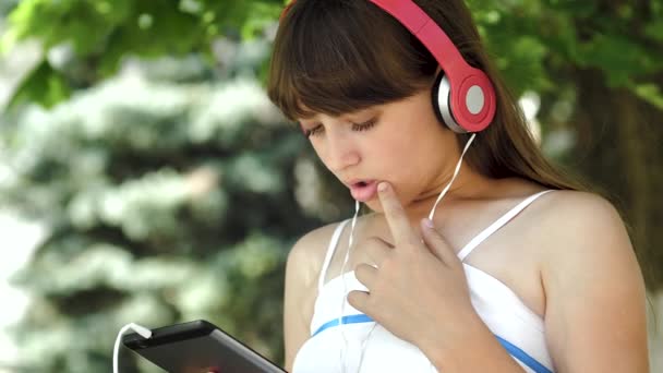 Chica joven en auriculares escuchando música en la tableta y caminando por la ciudad. Primer plano
 - Metraje, vídeo