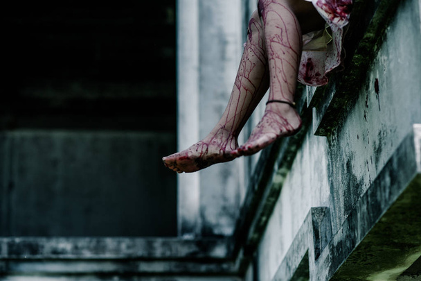 Horror Scene of a Woman with Bloody leg .Zombie woman  sitting hanging legs on building is screaming darkness and nightmare horror of scary fear on hell is  devil girl in halloween festival concept - Photo, image