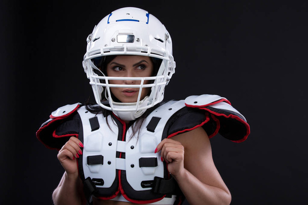 Portrait of sexy attractive young girl in a sports outfit for rugby with the helmet strongly looking forward standing on black background. Copy space - Photo, Image