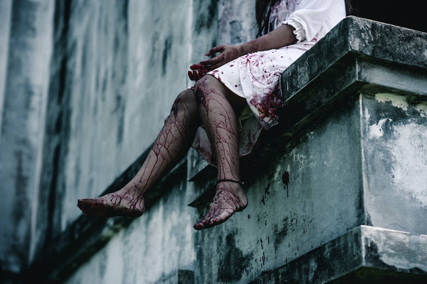 Horror Scene of a Woman with Bloody leg .Zombie woman  sitting hanging legs on building is screaming darkness and nightmare horror of scary fear on hell is  devil girl in halloween festival concept - Foto, afbeelding