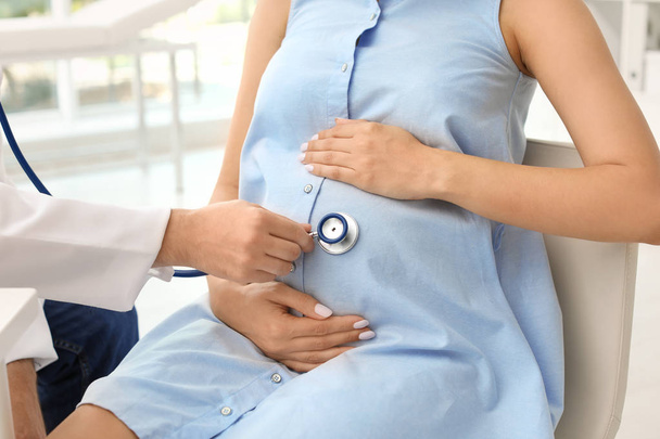Νεαρός γιατρός εξέταση έγκυος γυναίκα στο νοσοκομείο. Παροχή συμβουλών στους ασθενείς - Φωτογραφία, εικόνα