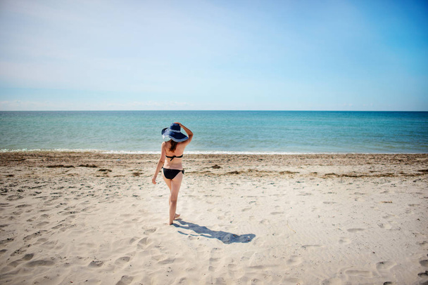hermosa chica en un sombrero azul, caminando por la playa
. - Foto, imagen
