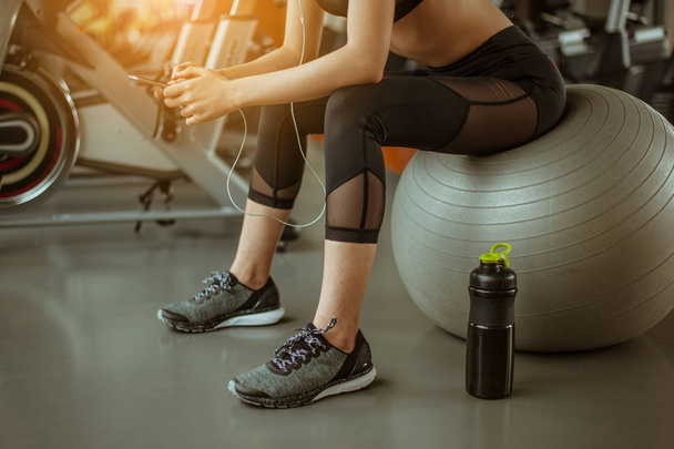 Fitness Girl sitting and listening to music on the ball at the fitness. - 写真・画像