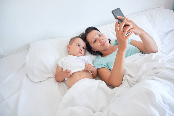 Máma a dítě spolu leží v posteli a pořizování autoportrétů - Fotografie, Obrázek