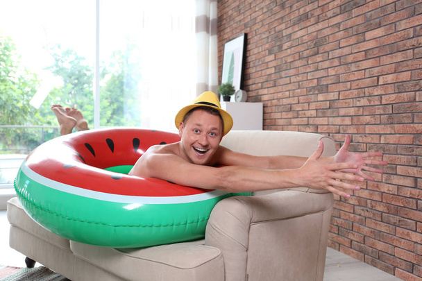 Shirtless man having fun with inflatable ring on sofa at home - Фото, изображение