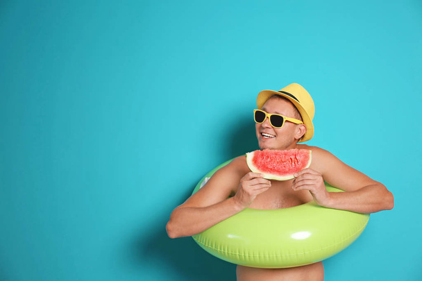 Мужчина без рубашки с надувным кольцом ест арбуз на цветном фоне
 - Фото, изображение
